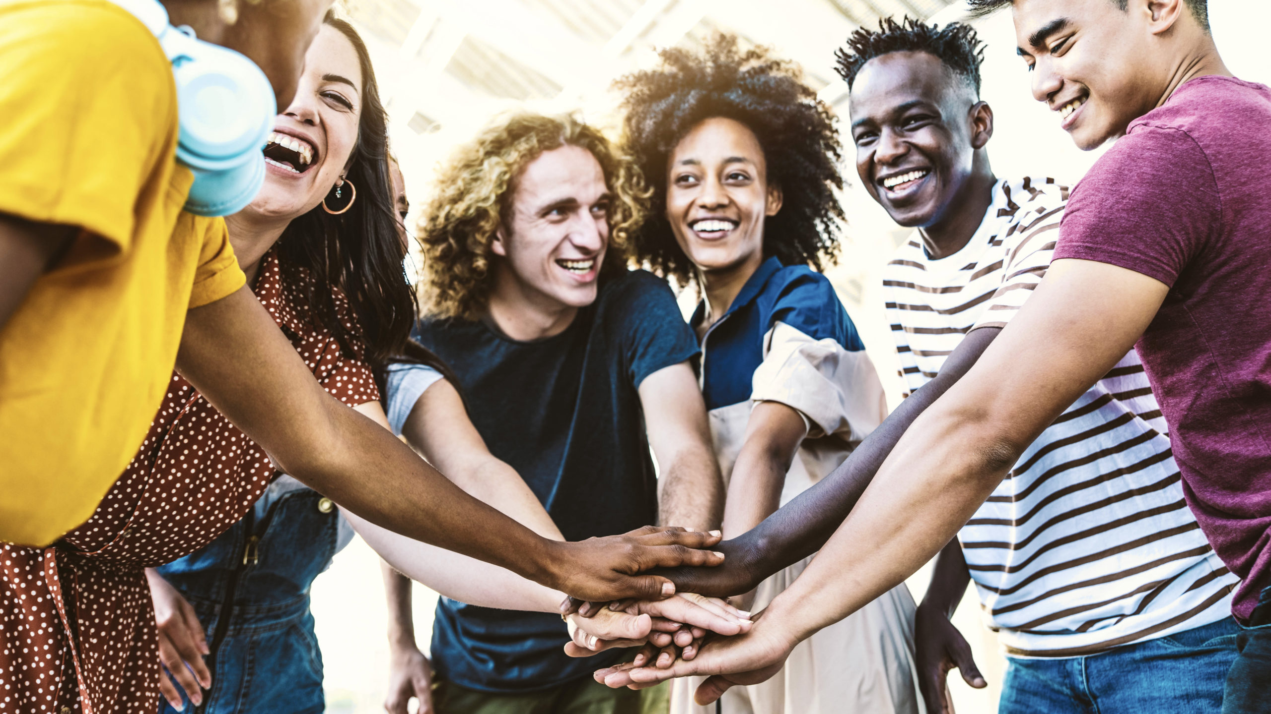 Multiracial happy young people putting their hands on top of eac Multiracial happy young people putting their hands on top of each other